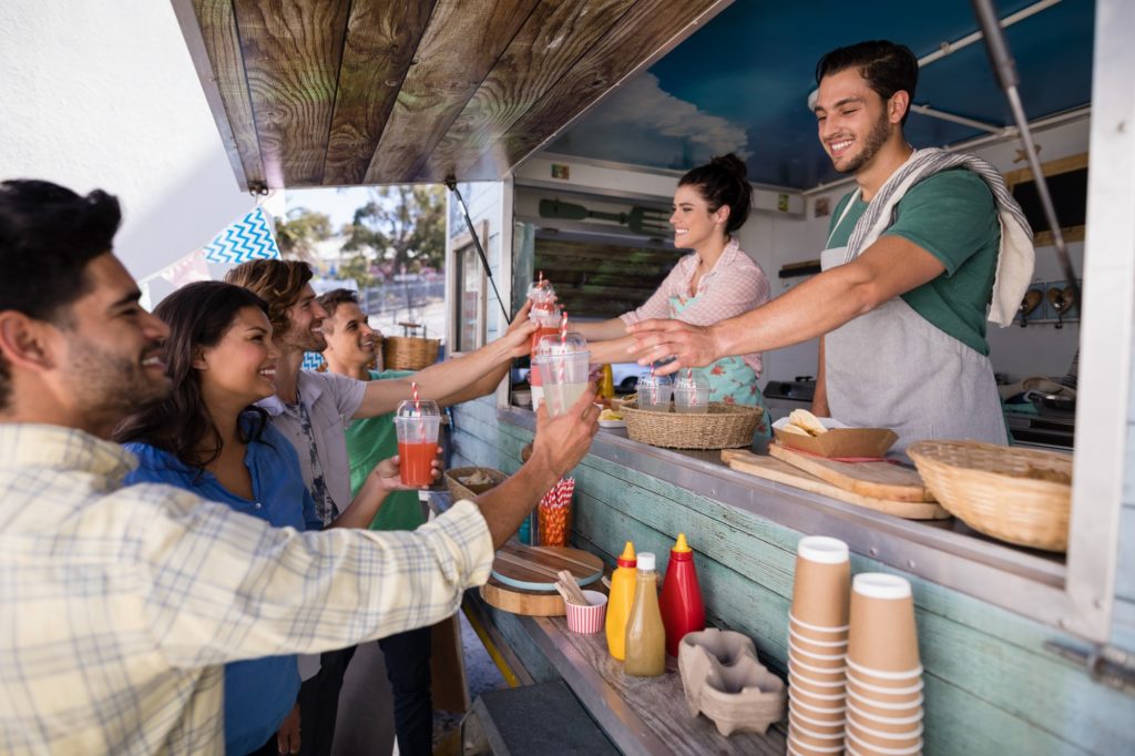 smiling food truck workers serve drinks to a group of young people from their food truck service window