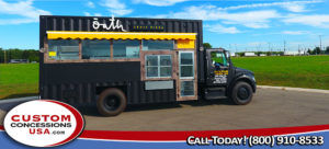 cool black food truck with small yellow awning parked in front of a green field