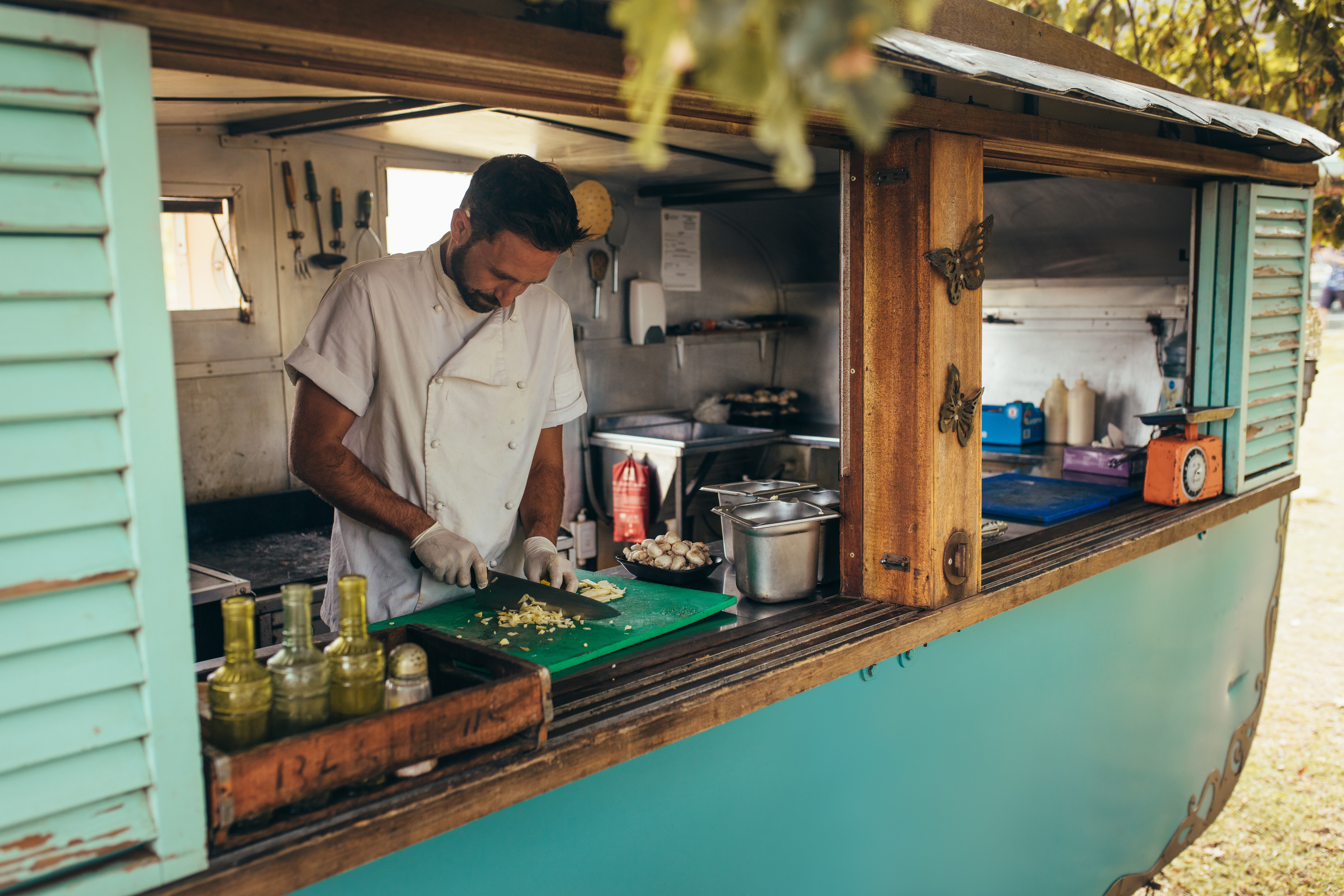 Man cooking some food in a mobile food truck parked under a tree. Man chopping vegetable on his food truck.