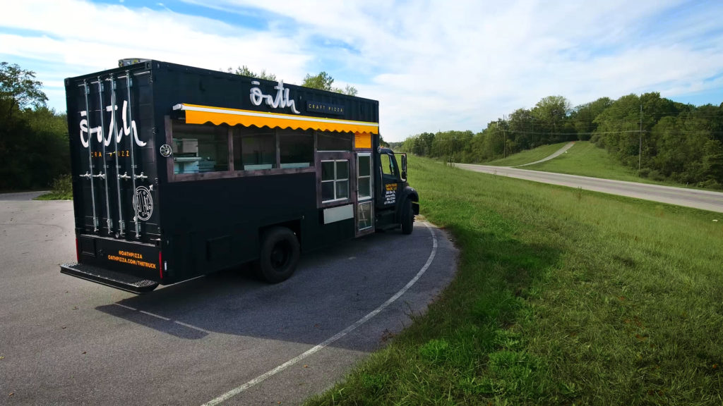 black food truck with yellow awning parked on blacktop near some grass