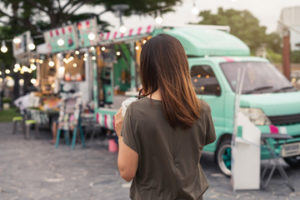 young woman walks past colorful food trucks with a smoothie in hand