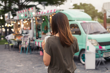 young woman walks past colorful food trucks with a smoothie in hand