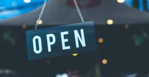 close up of an open sign hanging in a window with lights reflected in the background