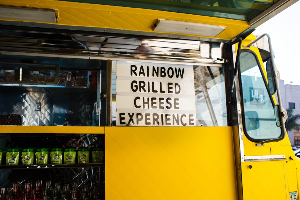 menu window on the side of a yellow food truck reads: rainbow grilled cheese experience