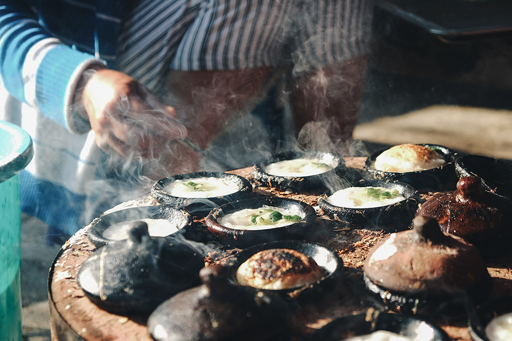 man leaning down over steaming bowls of Vietnamese food