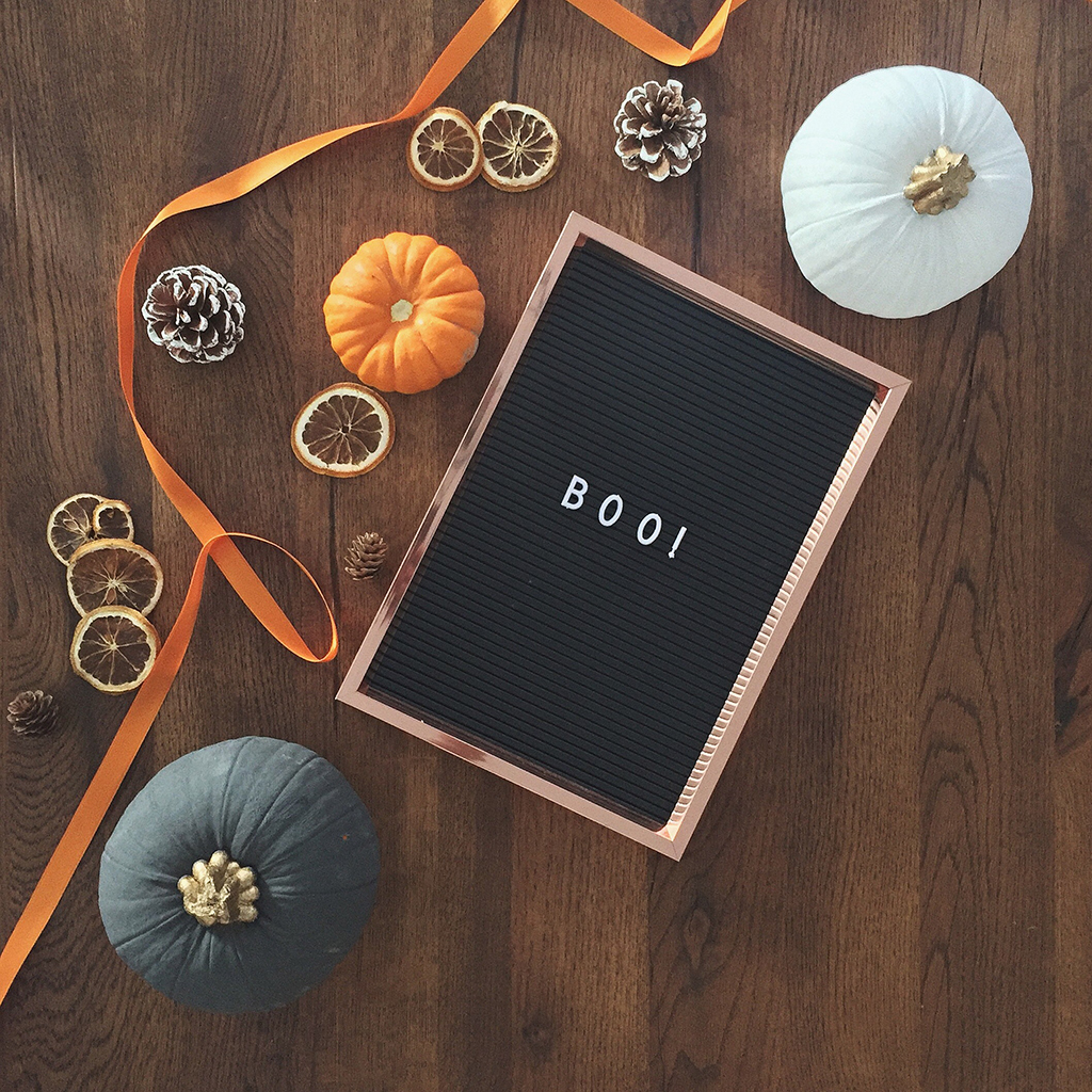 wooden table with fall decorations including pumpkins, dried orange slices, pinecones and a signboard with the word "boo" on it