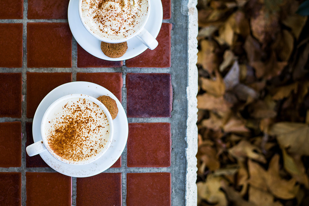 overhead view of two cups of coffee sitting on a tiled deck with autumn leaves in the background