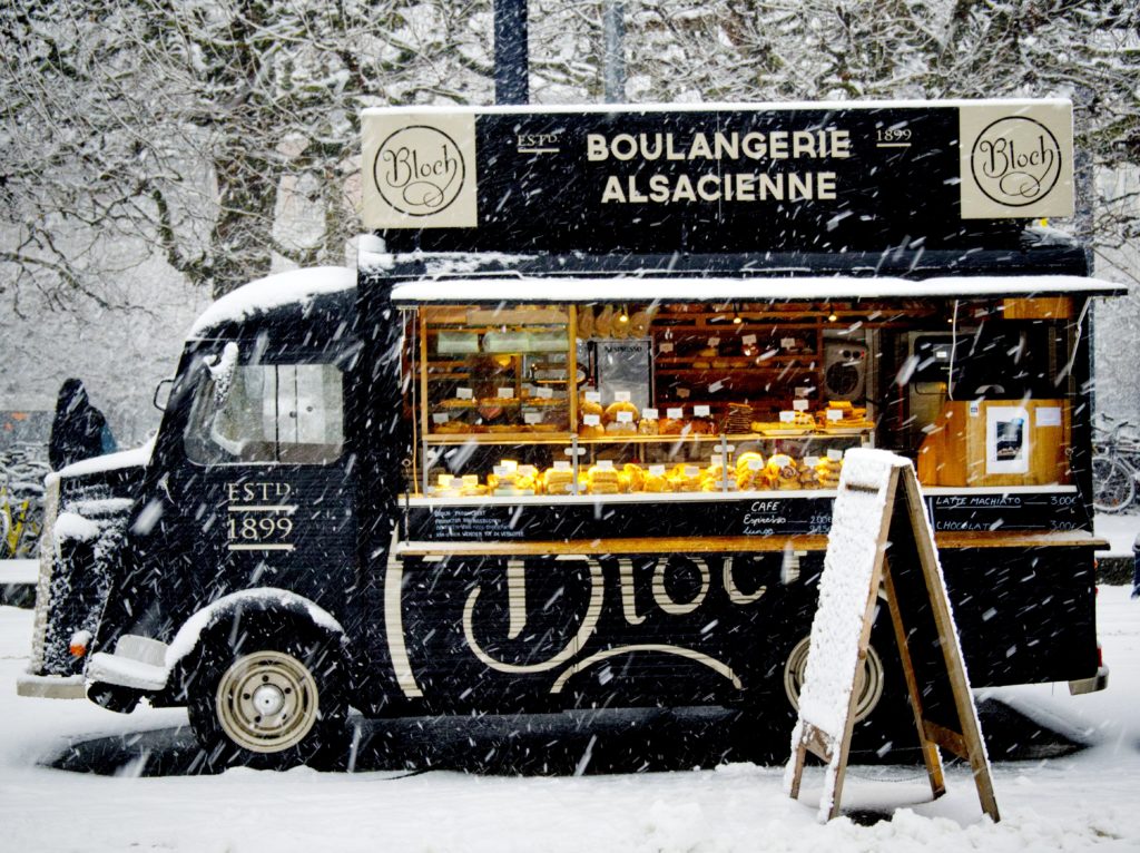 black vintage food truck selling baked goods in a snowy winter scene