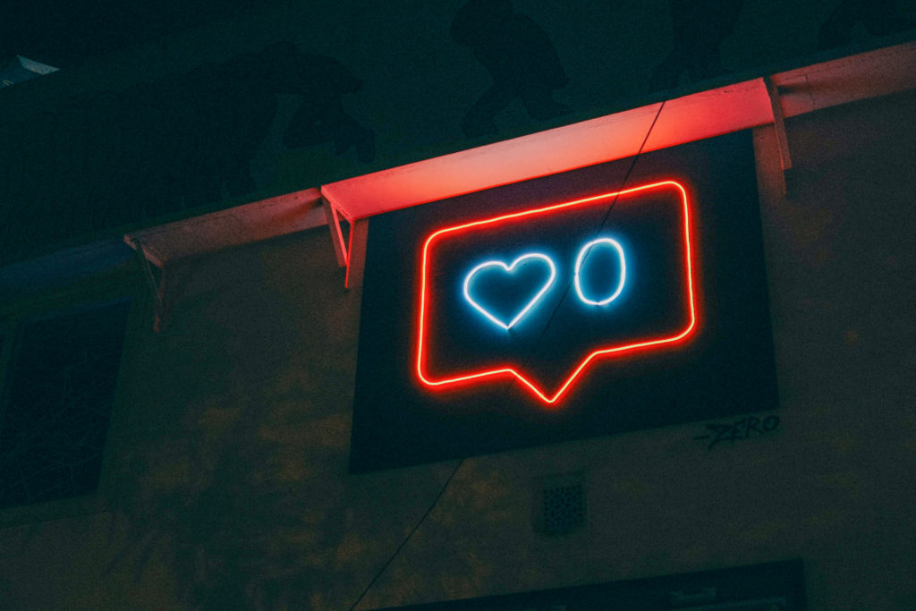 neon sign shaped like an Instagram like counter—a red comment box with a blue heart and a 0.