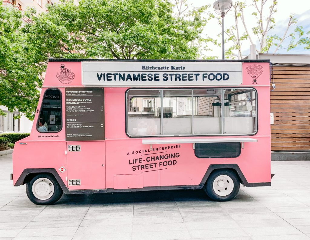 pink food truck selling Vietnamese street food parked on a city plaza