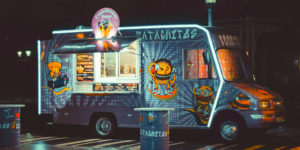 Photo of a blue burger food truck with neon lights parked under a streetlamp in a parking lot