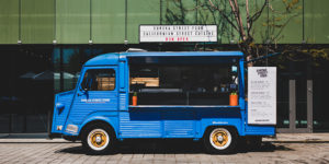 photo of a blue vintage food truck parked in front of urban building on a city street