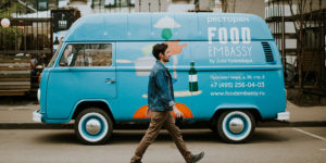 photo of a dark-haired man walking in front of a blue van food truck on a city street