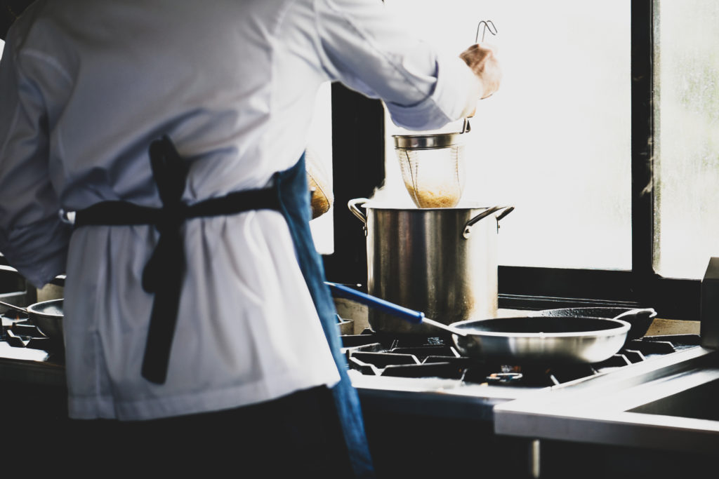 photo of a chef lowering a strainer full of noodles into a pot on a stove