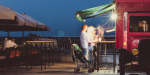 photo of motion-blurred man and woman with a stroller waiting in line under an awning at a red food truck