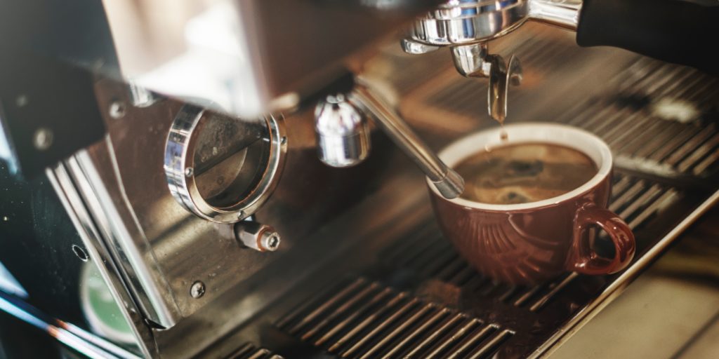 close up photo of espresso coffee dripping from an espresso machine into a small brown mug in a mobile coffee shop