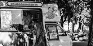 black and white photo of a gelato food truck in a park with customers discussing the menu
