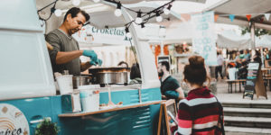 Photo of a woman waiting in front of a vintage blue and white food truck where a man is cooking crepes