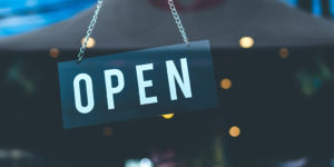 close up of an open sign hanging in a window with lights reflected in the background