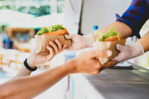 Close up photo of a food truck vendor with gloves on handing a customer two hot dogs.