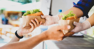 Close up photo of a food truck vendor with gloves on handing a customer two hot dogs.