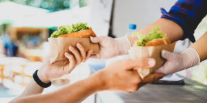 Close up photo of a food truck vendor with gloves on handing a customer two hot dogs.