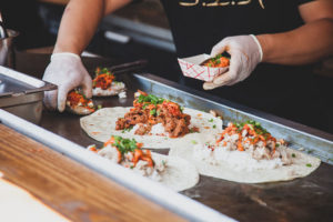 food truck chef preparing tortillas filled with rice and meat on a griddle