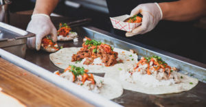food truck chef preparing tortillas filled with rice and meat on a griddle