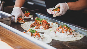 food truck chef preparing tortillas filled with rice and meat on a griddle