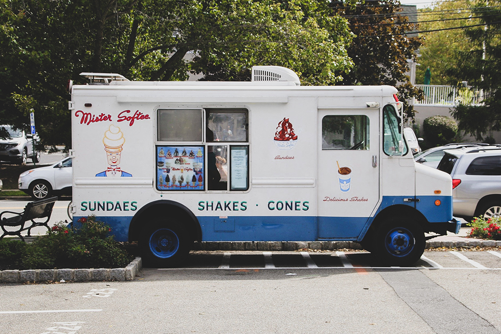 photo of a white and blue ice cream truck parked in a parking lot on a sunny day