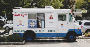 photo of a white and blue ice cream truck parked in a parking lot on a sunny day
