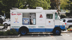 photo of a white and blue ice cream truck parked in a parking lot on a sunny day