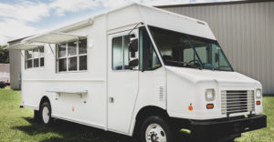 photo of a white food truck parked in grass in front of a warehouse