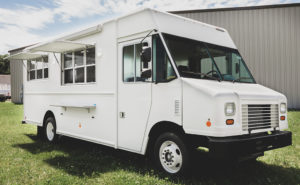 photo of a white food truck parked in grass in front of a warehouse