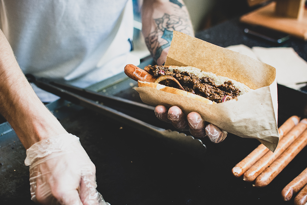 photo of hands with plastic gloves on preparing a hot dog over a cooktop