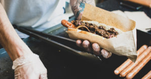 photo of hands with plastic gloves on preparing a hot dog over a cooktop