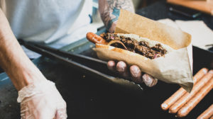 photo of hands with plastic gloves on preparing a hot dog over a cooktop