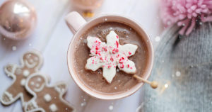 festive holiday photo of hot chocolate on a table with gingerbread, ornaments, and a winter hat