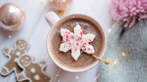 festive holiday photo of hot chocolate on a table with gingerbread, ornaments, and a winter hat