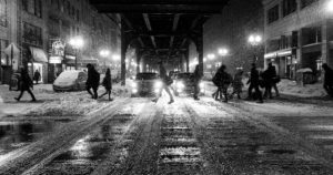 black and white photo of a snowy winter scene on urban street with pedestrians and cars