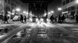 black and white photo of a snowy winter scene on urban street with pedestrians and cars