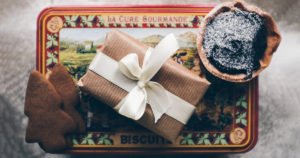 photo of a wrapped gift and cookies on top of a Christmas biscuit tin with snowy background