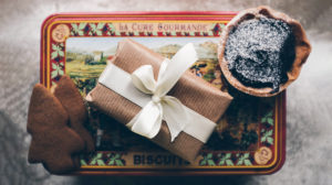 photo of a wrapped gift and cookies on top of a Christmas biscuit tin with snowy background