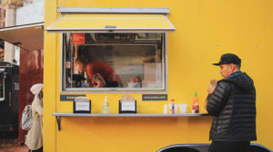 patrons getting food from a yellow food trailer