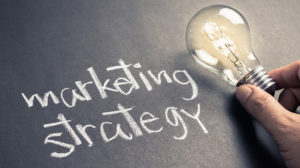 handwritten text that reads "marketing strategy" on chalkboard with glowing light bulb