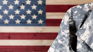 Close up of military uniform with painted rustic boards of USA flag in background.